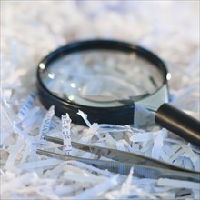 Confidential paperwork shredded with a magnifying glass and tweezers.