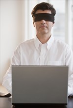 Businessman using laptop while blindfolded.