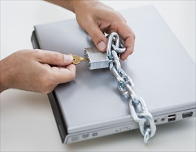 Hands placing lock and chain on computer.