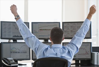 Male trader raising arms in success.