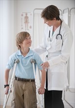 Female doctor assisting boy on crutches.