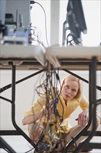 Woman under table working on networked computers.