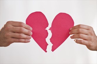 Two hands holding broken paper heart.