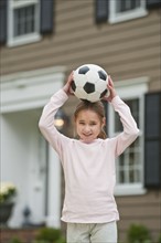 Girl holding soccer ball on head.