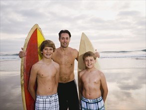 Father and sons standing with surfboards