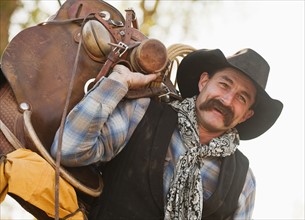 Cowboy holding saddle.