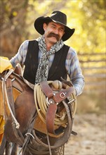 Cowboy holding saddle.