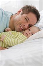 Father and baby lying down on bed.