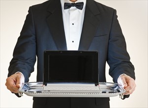 Butler holding laptop on tray.