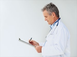 Doctor writing on clipboard. Photographer: momentimages