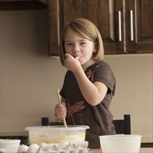 Young girl tasting cookie batter. Photographer: Mike Kemp
