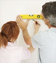 Couple marking a straight line on wall. Photographer: momentimages