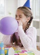Young girl blowing up balloon. Photographer: Jamie Grill
