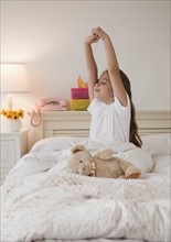 Young girl stretching in bed. Photographer: Jamie Grill