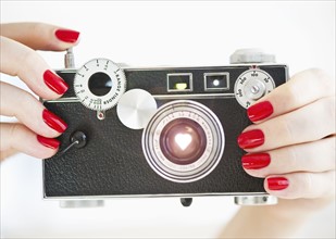 Antique camera being held by woman wearing red nail polish.