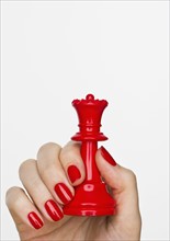 Hand holding red queen chess piece.