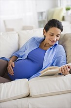 Pregnant woman reading on couch.
