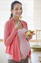 Pregnant woman eating bowl of fruit.