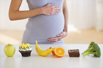 Pregnant woman standing behind a row of food.