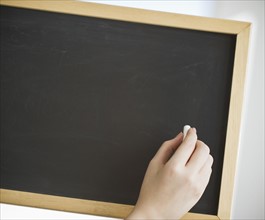 Hand holding chalk in front of blank chalkboard.