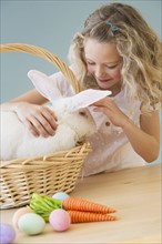 Young girl petting a rabbit in a basket.