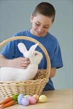 Young boy petting a rabbit in Easter basket.