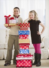 Young children beside a stack of Christmas gifts.