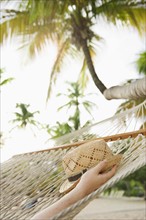 Hand holding straw hat in hammock. Photographe : Jamie Grill