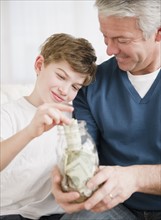Father and son putting money in jar. Photographe : Jamie Grill