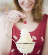 Woman putting a cherry on top of ice cream. Photographe : Jamie Grill