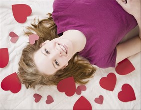 Woman lying amongst red hearts. Photographe : Jamie Grill