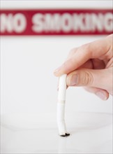 Hand putting out cigarette in front of no smoking sign. Photographe : Jamie Grill