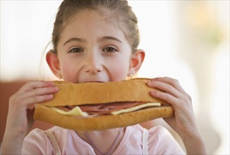 Young girl eating a large sandwich. Photographe : Daniel Grill