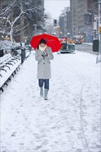 Woman walking with red umbrella on snowy day. Photographe : Daniel Grill