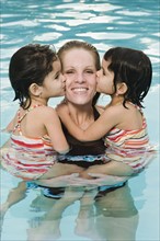 Mother holding daughters in pool.