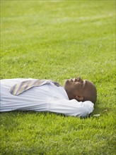 Businessman lying on grass.