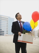 Businessman holding box and balloons.