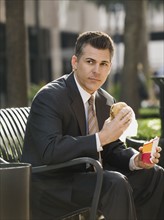Businessman eating lunch on park bench.