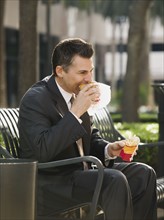 Businessman eating lunch on park bench.