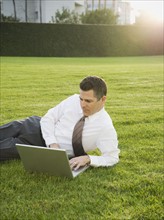Businessman relaxing with laptop on lawn.