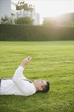 Businessman texting while lying on grass.