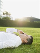 Businessman lying on grass while talking on phone.