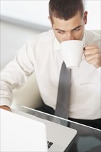 Businessman drinking coffee at desk. Photographe : momentimages