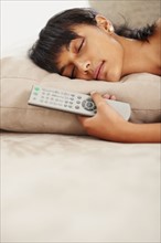 Young woman holding remote control while sleeping. Photographe : momentimages