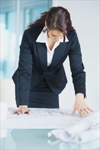 Businesswoman looking at blueprints. Photographe : momentimages