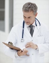 Doctor looking at clipboard. Photographe : momentimages