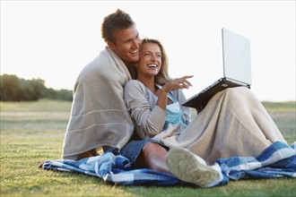 Couple looking at laptop outdoors. Photographe : momentimages