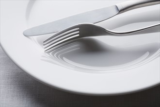 Fork and knife on empty white plate. Photographe : Kristin Lee