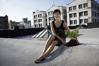 Woman sitting on rooftop beside aspen sapling. Photographe : Shawn O'Connor