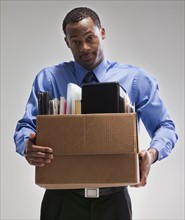 Businessman holding a box of office supplies. Photographe : Mike Kemp